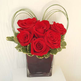 Red roses arranged in a clear square vase with arched greenery