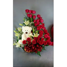 Red roses and white lilies arranged with a teddy bear in a basket