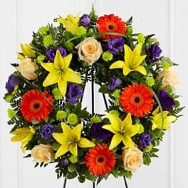 Circular floral wreath with yellow lilies, orange gerberas, and cream roses