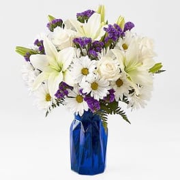 White lilies and daisies with purple filler in a blue vase