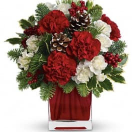 Red and white floral arrangement in a clear vase with pinecones and berries