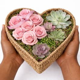 Heart-shaped woven box filled with pink roses and succulents held in two hands