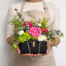 Compact arrangement of pink roses, white blooms and green hydrangea in a black purse-style container