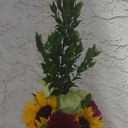 Sunflowers, roses, and carnations in a black vase with tall greenery