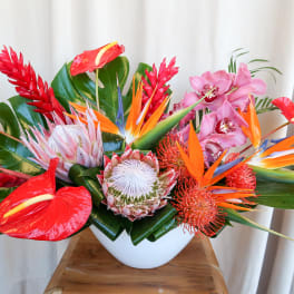 Tropical flower arrangement in a white bowl vase with red, orange, pink, and white blooms