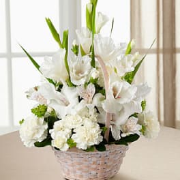White floral arrangement in a woven basket with tall green leaves
