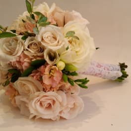 Bouquet of pale roses and peach flowers with greenery, wrapped in lace
