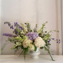 White vase with lavender and white flowers and trailing greenery