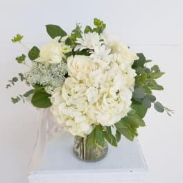 White floral bouquet in a glass vase with green foliage