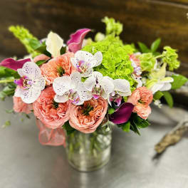 Bouquet of coral roses, white orchids, and green hydrangeas in a glass vase