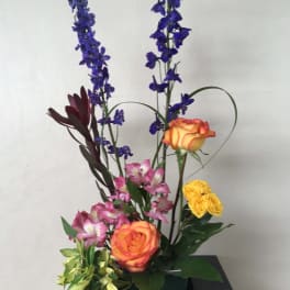 Tall floral arrangement with orange roses, pink alstroemeria, and blue delphinium