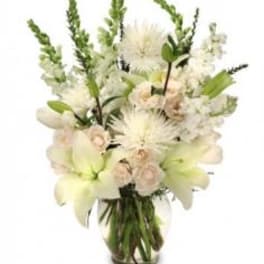 White floral arrangement in a glass vase with lilies and spiky blooms