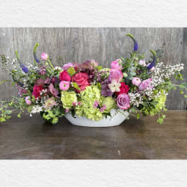 Low floral centerpiece with pink and purple blooms in a white bowl vase