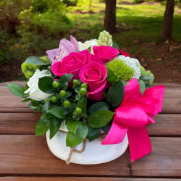 Pink and white rose arrangement in a white bowl with a bright ribbon
