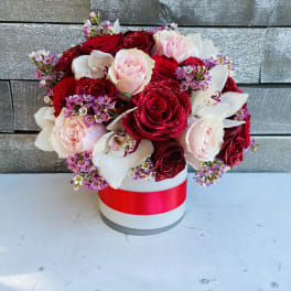 Bouquet of red and blush roses with white orchids in a round box