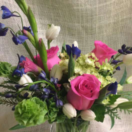 Bouquet of pink roses, white tulips, and blue flowers in a glass vase