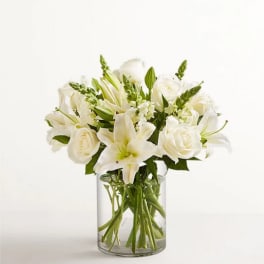 White lilies and roses arranged in a clear glass vase