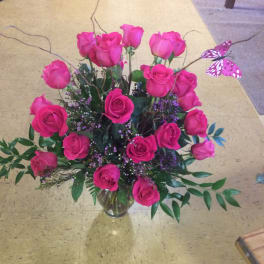 Tall arrangement of hot pink roses with curly branches and a pink butterfly in a clear glass vase
