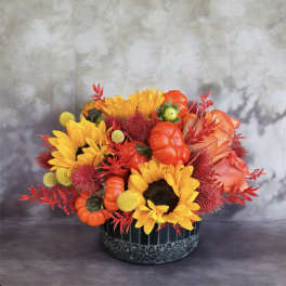 Sunflower arrangement with orange pumpkins in a black container