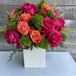 Pink and coral roses arranged in a white square vase