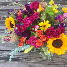 Bright mixed arrangement with sunflowers, hot pink and orange roses in a clear glass vase on a wooden surface