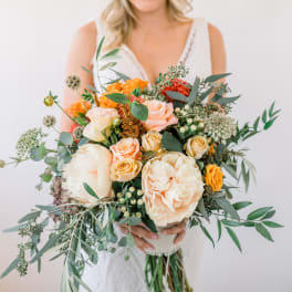Bride holding a bouquet of peach and orange roses with greenery