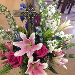 Floral arrangement with pink lilies, hot pink roses, and a wooden cross