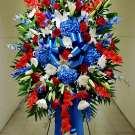 Large standing floral spray with red, white, and blue flowers and a blue ribbon