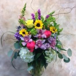 Mixed bouquet with sunflowers, purple orchids, and pink blooms in a glass vase