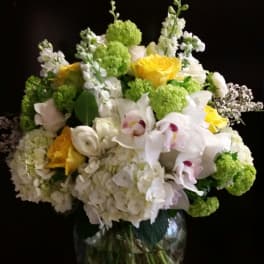 Mixed bouquet of white, yellow, and green flowers in a glass vase