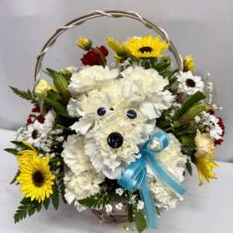Basket arrangement with white carnation dog, yellow sunflowers, red and white daisies and a blue bow
