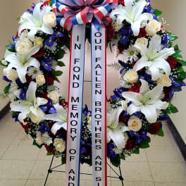Large memorial wreath with white lilies, roses, and blue flowers on a stand