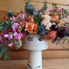 Mixed bouquet in a white face vase with pink, peach, and purple flowers