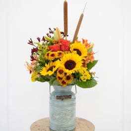 Sunflower and rose arrangement in a blue metal container with cattails