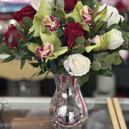 Red and white roses with green orchids in a mirrored vase