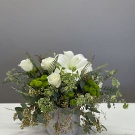 White roses and lilies in a gray container with trailing greenery