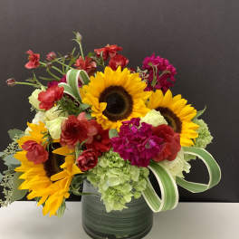 Mixed bouquet with sunflowers, hydrangeas, and red blooms in a dark vase