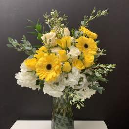 Yellow gerbera daisies and white roses in a glass vase