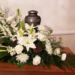 White funeral spray with lilies and roses around a black urn
