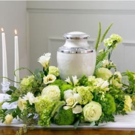Green and white funeral floral arrangement with an urn centerpiece