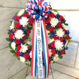 Standing floral wreath with red, white, and blue flowers and a memorial ribbon