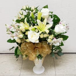 White roses and lilies arranged in a white vase with a gold bow