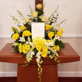 Yellow and white floral funeral arrangement with a central plaque