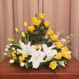 Yellow roses and white lilies arranged in a low centerpiece with a silver vase