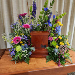 Colorful funeral floral arrangement around a wooden urn pedestal