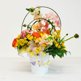 Mixed flower arrangement in a white bucket with ribbon and wire loops