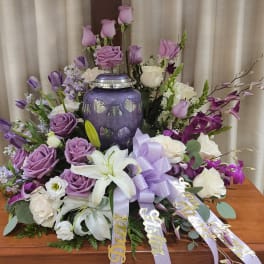 Purple and white floral funeral arrangement with a butterfly urn centerpiece