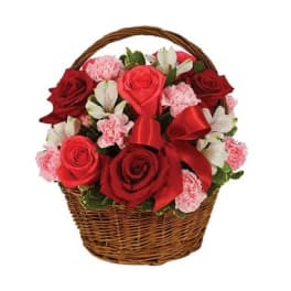Basket of red roses, pink carnations, and white flowers with a red ribbon