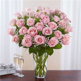 Pink roses arranged in a clear glass vase with a gift box and champagne flutes nearby