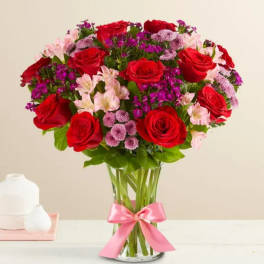 Bouquet of red roses and pink flowers in a clear glass vase with a pink ribbon